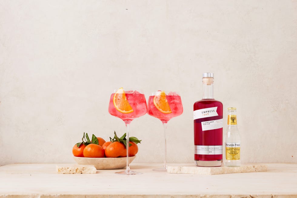 pink cocktails two blossom and tonic cocktails in wine glasses with mandarin slice garnishes next to a bowl of mandarins