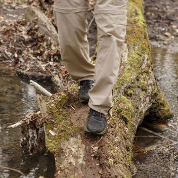 bottom half of a man crossing a creek on moss covered log in nature