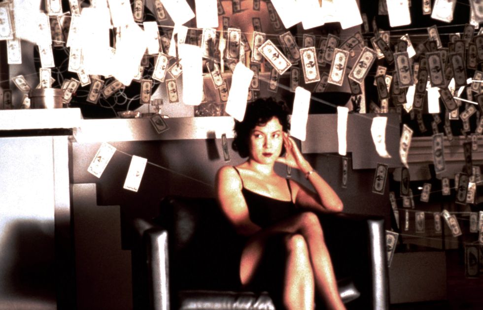 a brunette woman sitting in a room filled with money hanging on clotheslines
