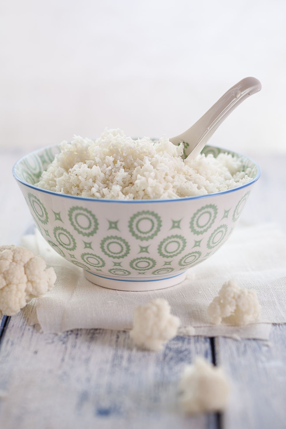 Bowl of cauliflower rice and cauliflower florets on cloth and wood