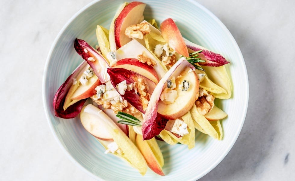 A bowl of endive salad with slices of apple, walnuts, and blue cheese on white background