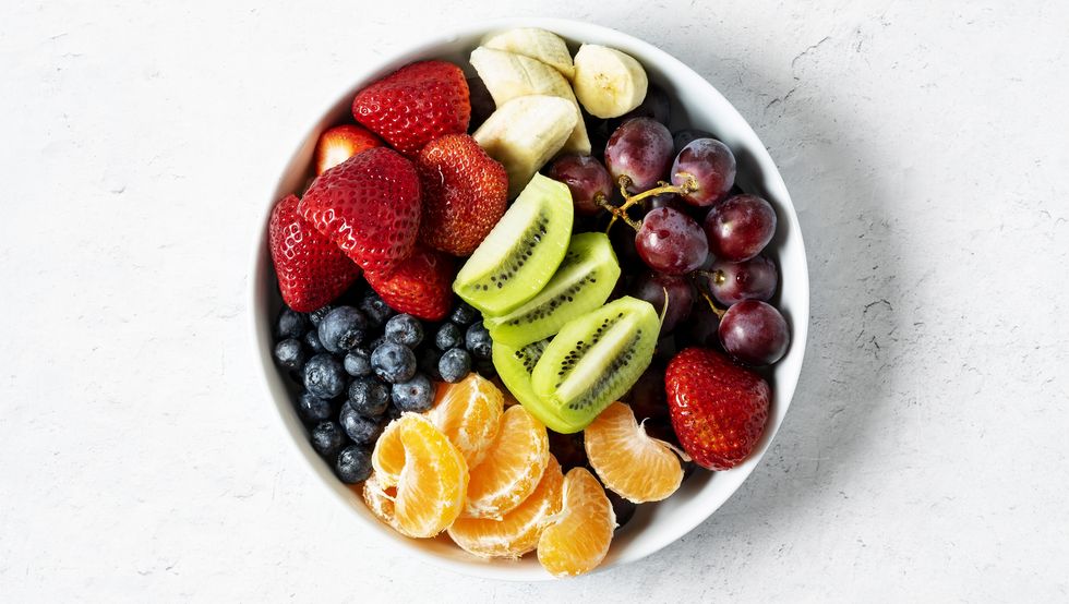 bowl of fresh fruit grapes, bananas, strawberries, grapes, oranges, and kiwi on white background
