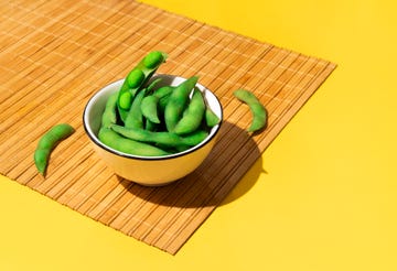 bowl of fresh soybeans edamame on a bamboo tablecloth on yellow colored background