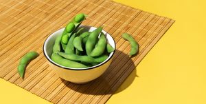 bowl of fresh soybeans edamame on a bamboo tablecloth on yellow colored background