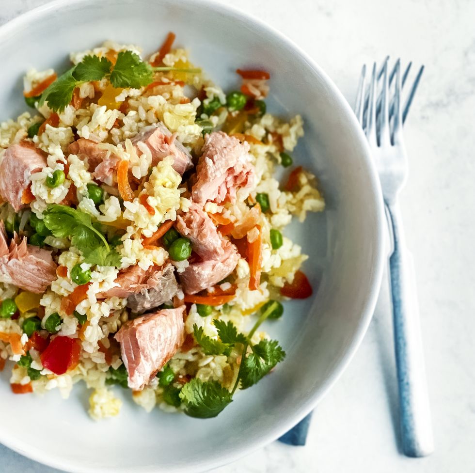 bowl of fried rice with vegetables and salmon on white background