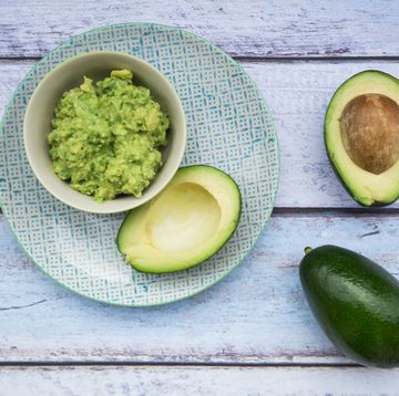 bowl of guacamole and whole and sliced avocados on light blue wood