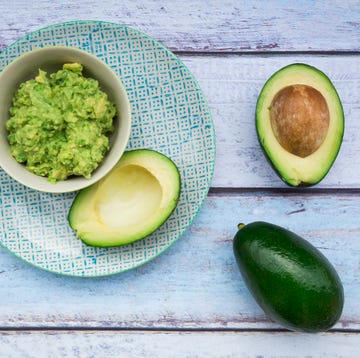 bowl of guacamole and whole and sliced avocados on light blue wood