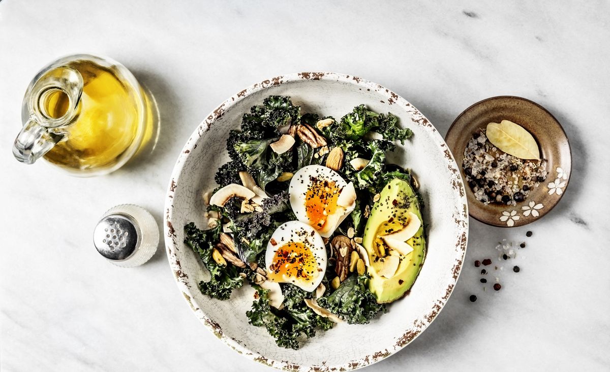Bowl of kale salad with boiled eggs and avocado on white background