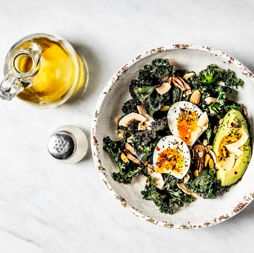 bowl of kale salad with boiled eggs and avocado on white background