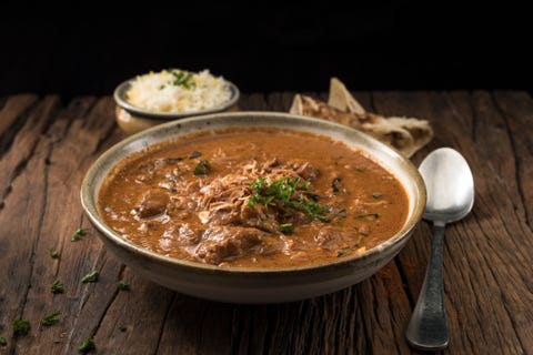 a bowl of lamb curry served with naan bread and rice