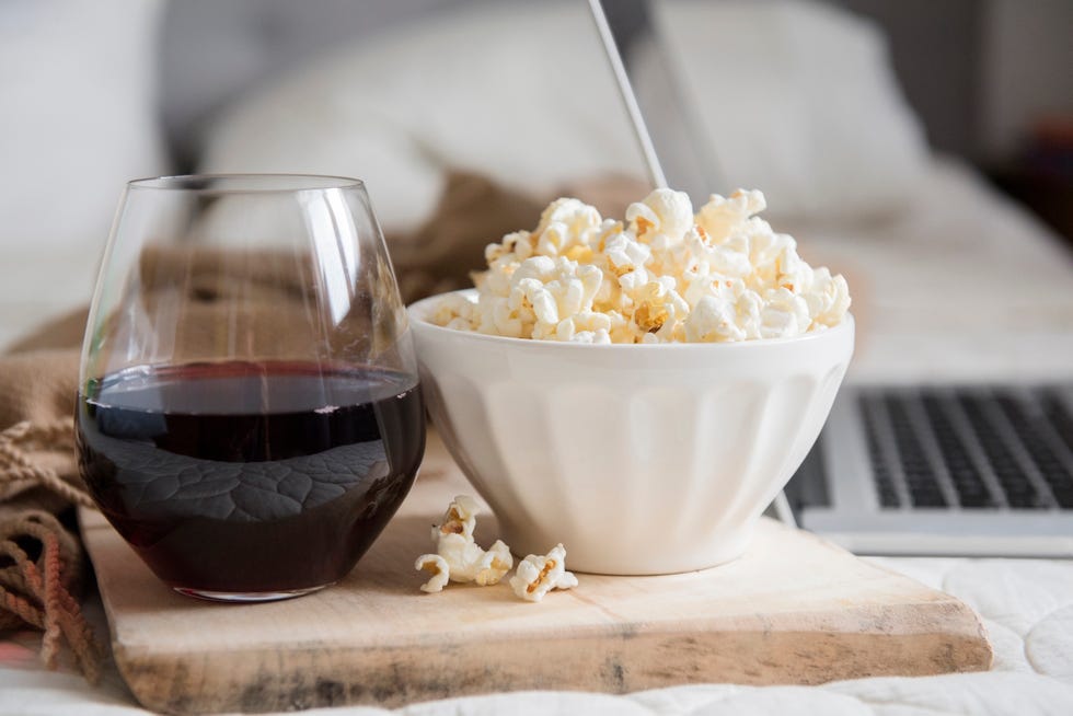 Bowl of popcorn and glass of wine near laptop