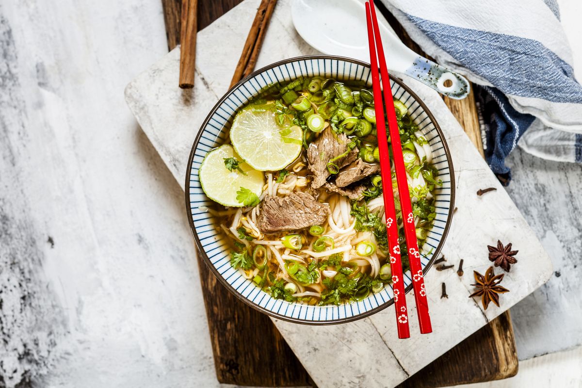 Bowl of Vietnamese Pho with rice noodles, mung beans, cilantro, spring onions and limes