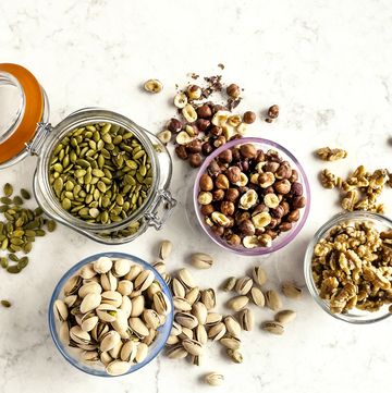 bowls and jars with seeds and nuts pistachios, walnuts, hazelnuts, and pumpkin seeds on white background