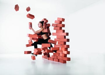 female runner wearing black pants top breaking through a brick wall.