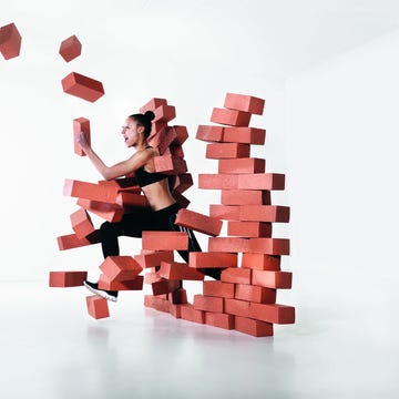 Runner shattering barrier female runner wearing black pants top breaking through a brick wall.