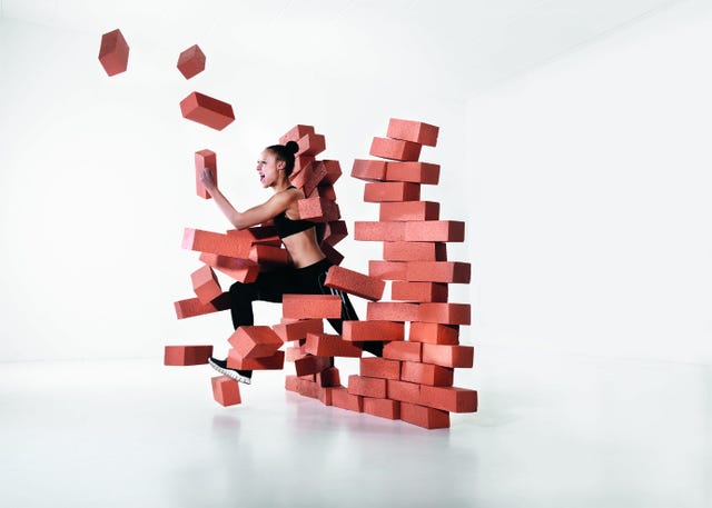 female runner wearing black pants top breaking through a brick wall.