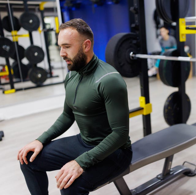 male athlete sitting and resting after lifting weight on bench press in the gym