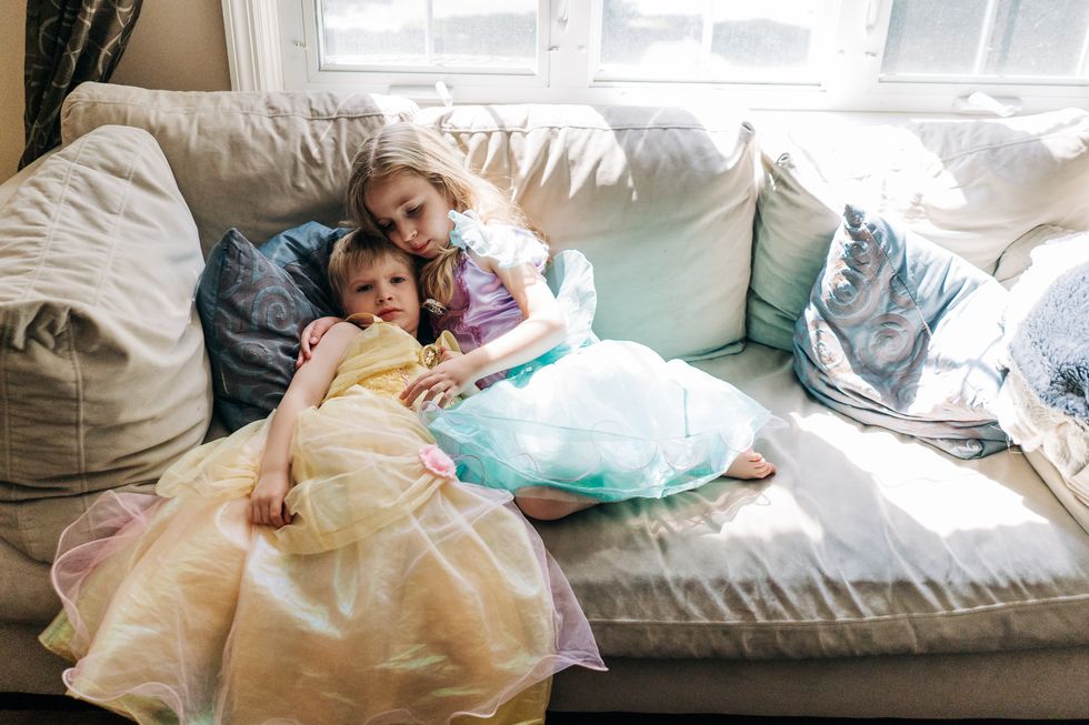 a boy and girl dressed in princess dresses sit on a couch