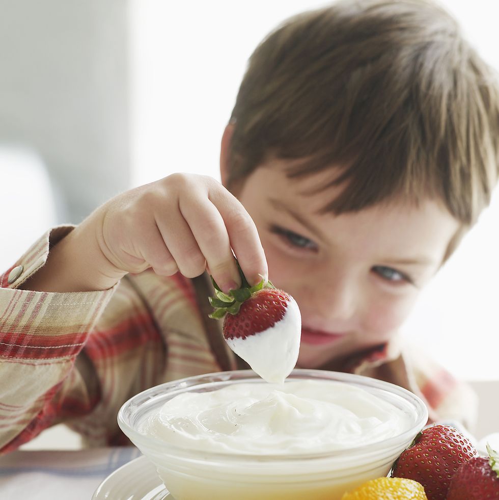 boy dipping strawberry in yogurt