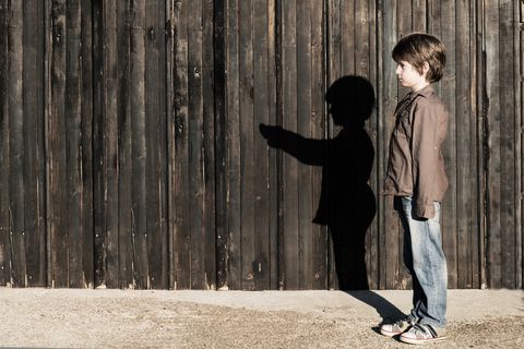 Boy standing next to a wooden fence with alter ego shadow
