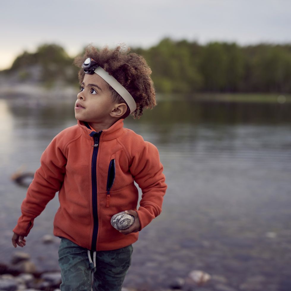 boy wearing headlamp holding rock at beach during sunset during a game of flashlight tag, a good housekeeping pick for best camping activity