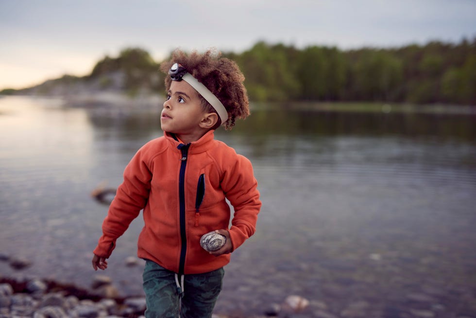 boy wearing headlamp holding rock at beach during sunset during a game of flashlight tag, a good housekeeping pick for best camping activity