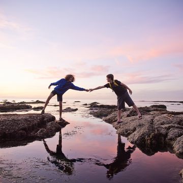 boys help each other across tidal pools at sunset