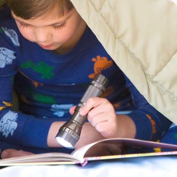 boy in dinosaur pajamas reading a book under the blanket