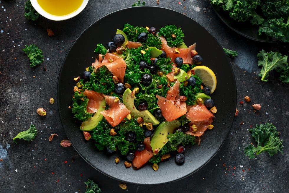 Salmon Kale Super Food salad with avocado, pistachio nuts and blueberries on black plate