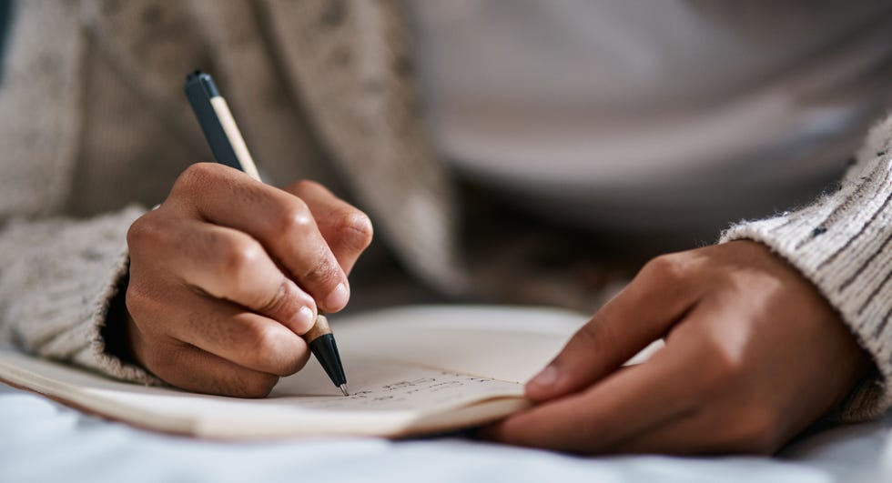 cropped image of a man jotting in a notebook on his bed at home