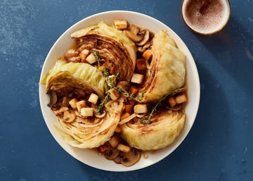 white bowl of braised cabbage with mushrooms, croutons, and fresh thyme on a dark blue background