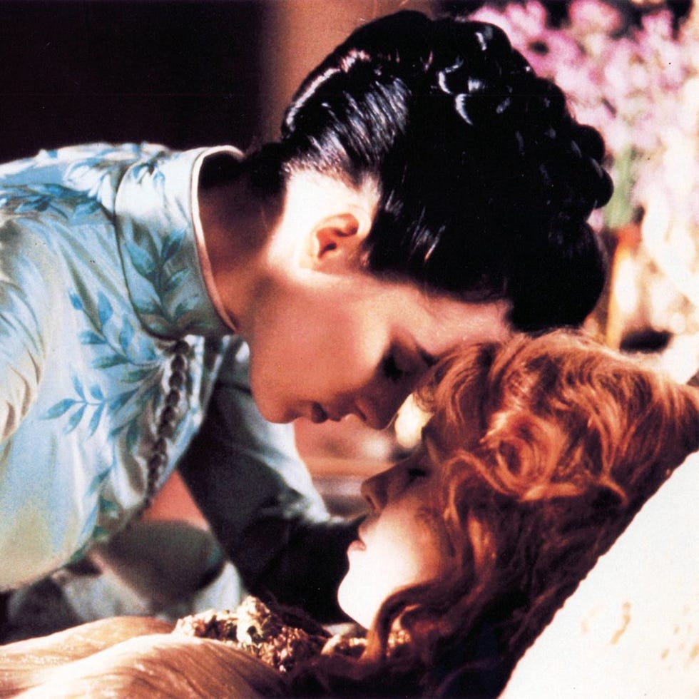 two women in intimate proximity with one in a traditional outfit and the other with wavy hair