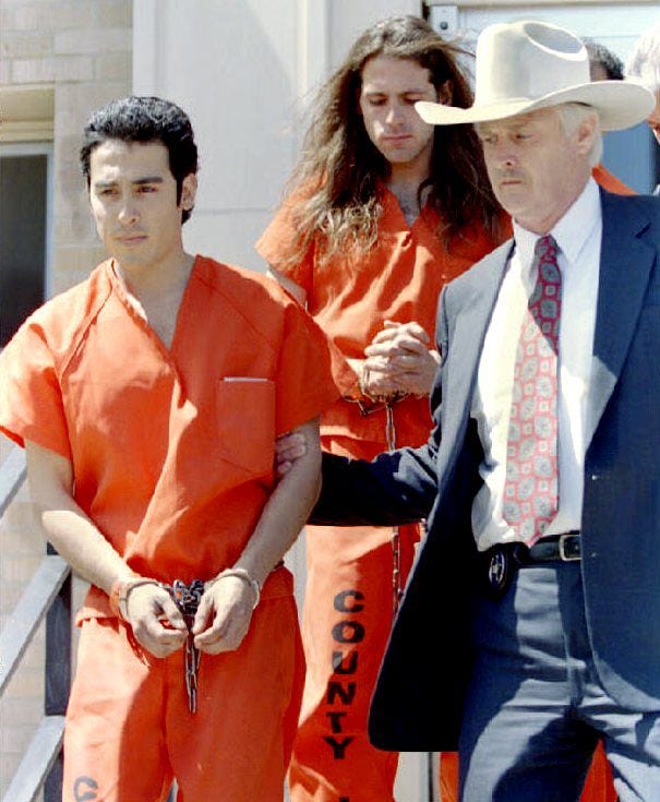 a man wearing a blue suit and cowboy hat escorts two inmates in orange jumpsuits down a flight of stairs outside