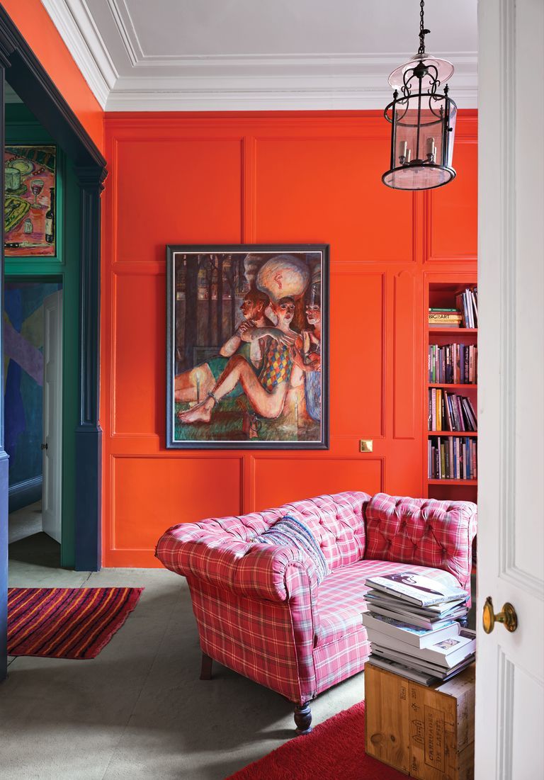 Den with orange walls and a pink plaid sofa