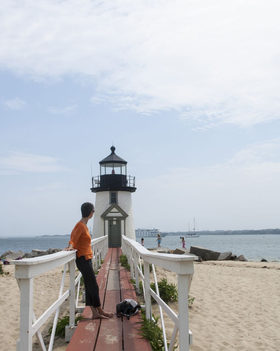 woman on walkway over beach leading to lighthouse with figures in the background