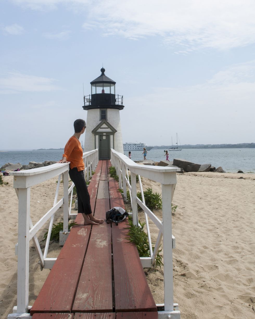 woman on walkway over beach leading to lighthouse with figures in the background