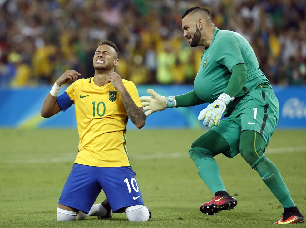 neymar kneels on a soccer field with his arms up, he is overcome with emotion and his eyes are shut, on his right weverton pereira da silva approaches with a smile on his face, both men wear soccer uniforms