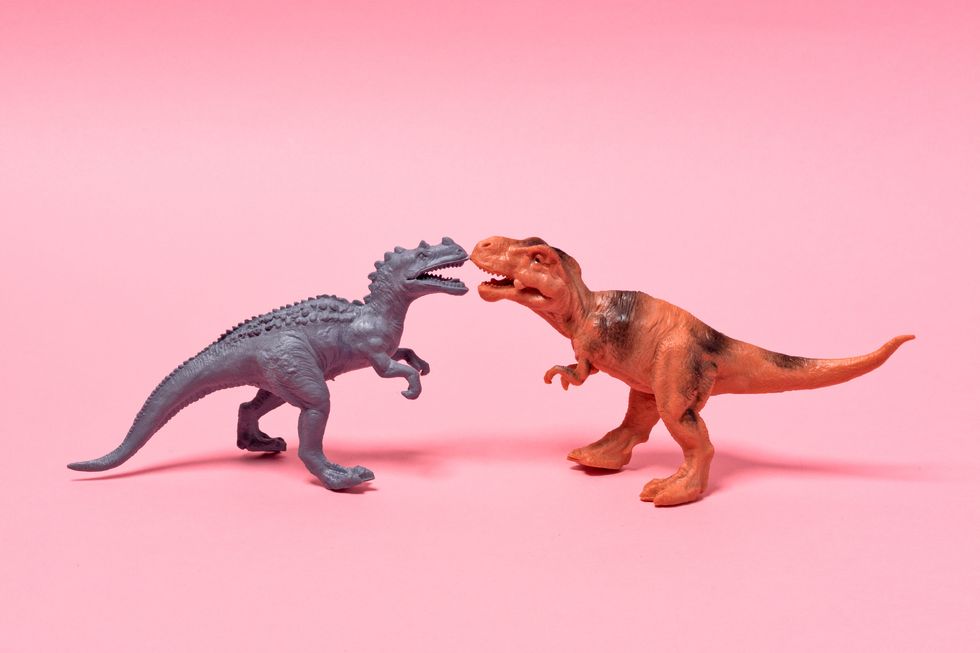 two toy dinosaurs face to face on pink background