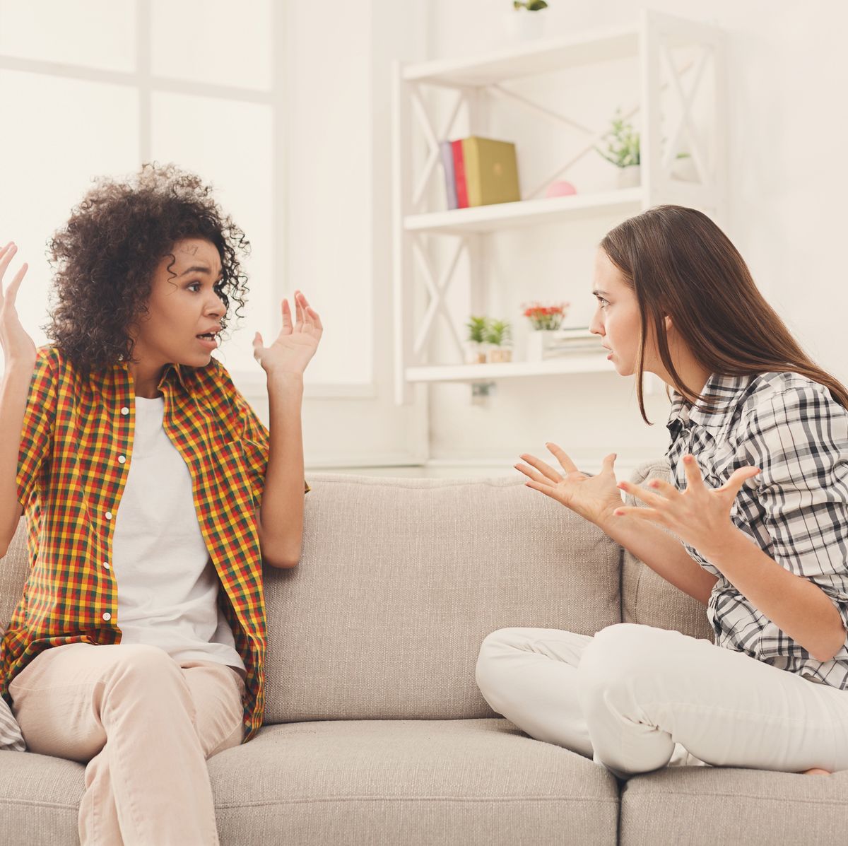 Two female friends sitting on sofa and arguing