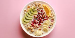 breakfast cereal meal granola with milk, pomegranate, kiwi and orange in bowl over pink background