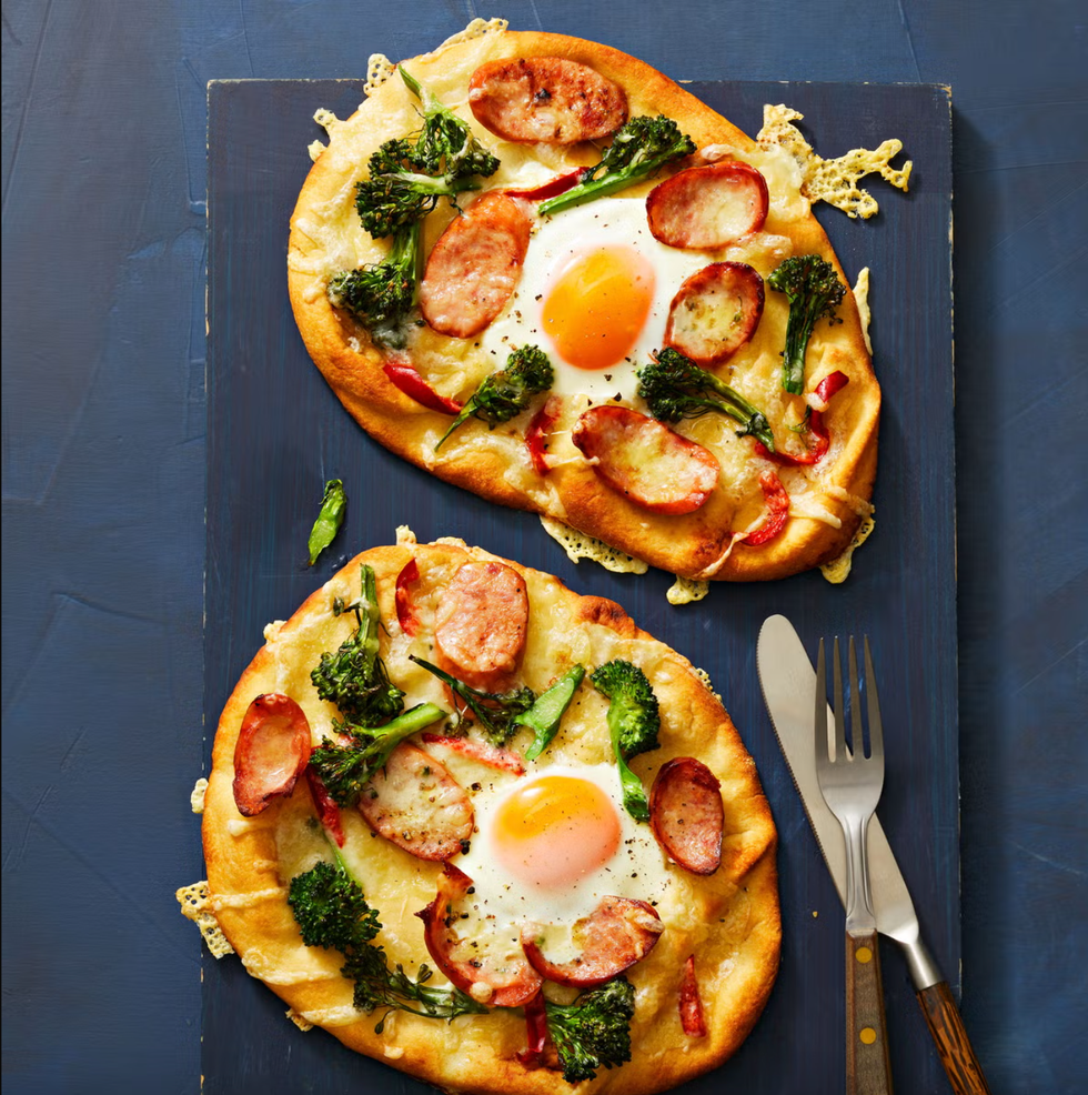naan topped with kielbasa, broccolini, and fried eggs with a fork and knife
