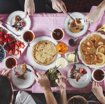 breakfast table flat lay of eating peoples hands over breakfast table with crepes, pancakes, tea and berries