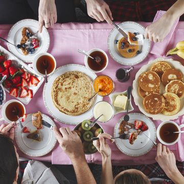 breakfast table flat lay of eating peoples hands over breakfast table with crepes, pancakes, tea and berries