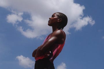 a confident individual standing against a blue sky with clouds arms crossed