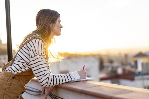 young woman taking notes on roof terrace at sunset