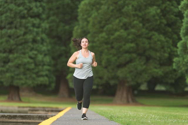 woman running down road with trees behind her