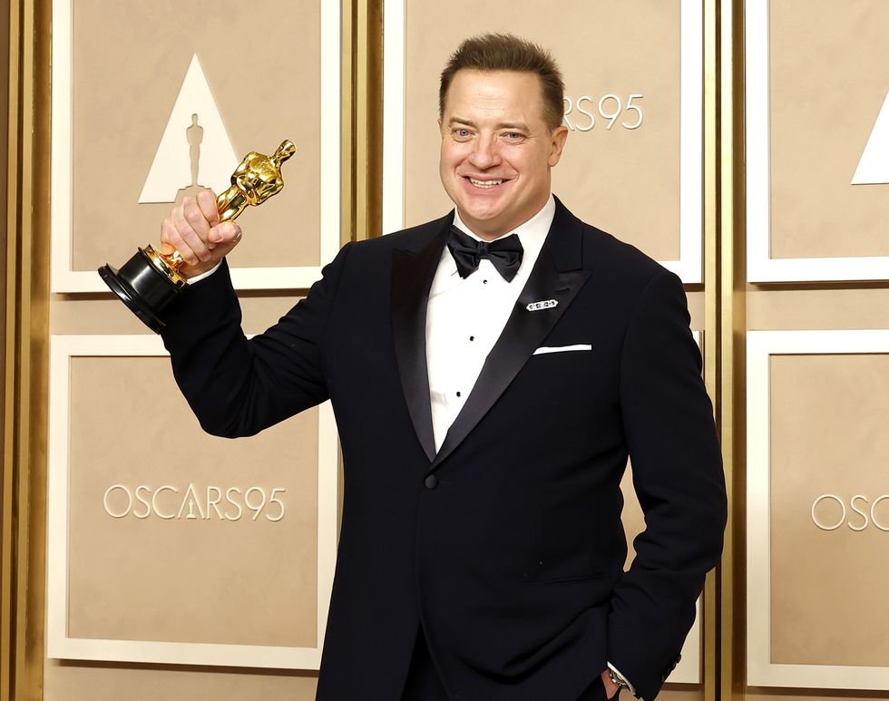 brendan fraser raising his academy award statuette with his right arm and smiling