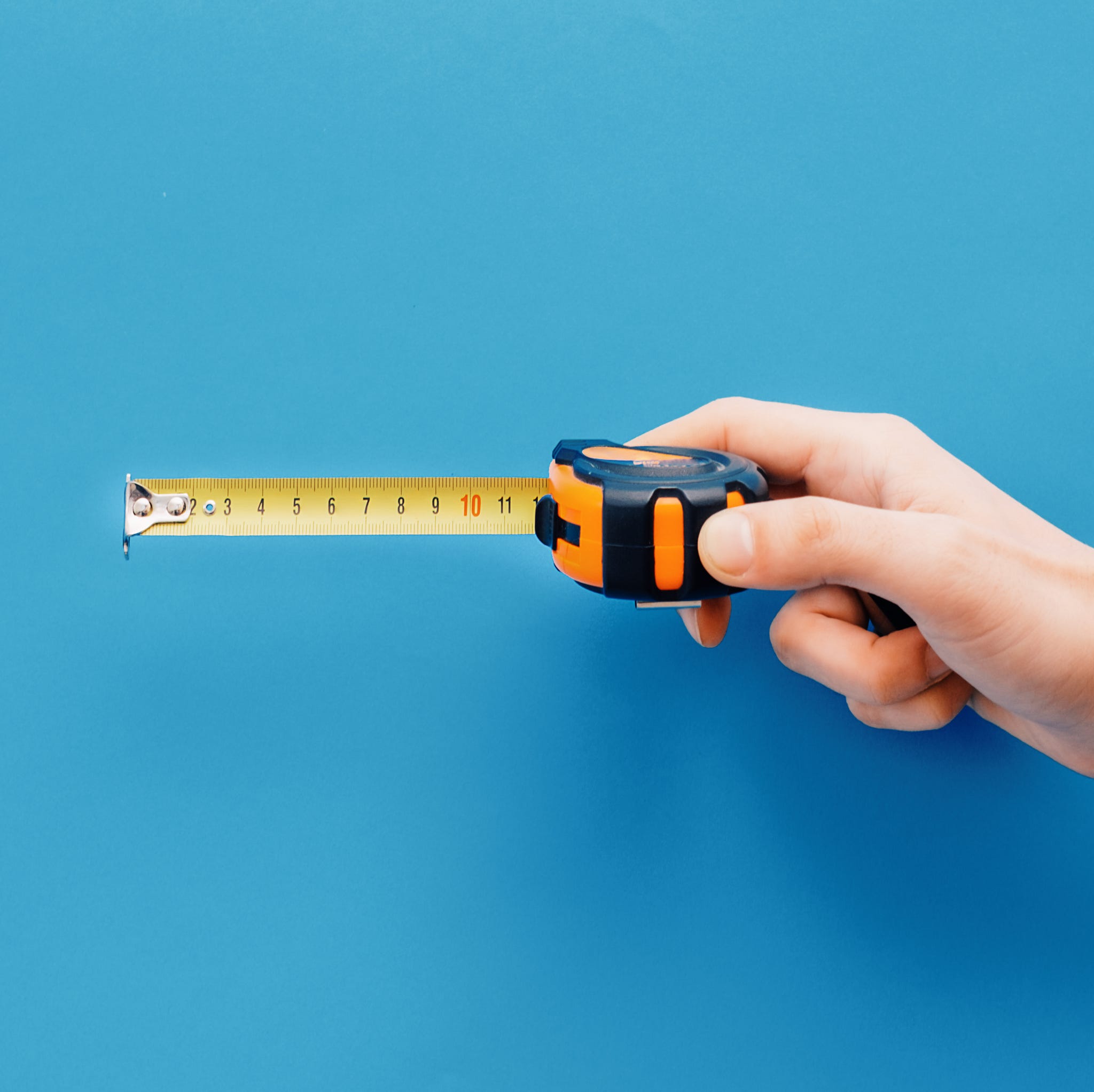 Bricolage concept.Hand holding tape measure on blue background