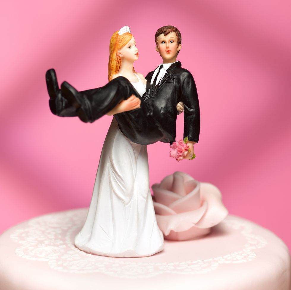 bride and groom wedding figurines where the bride is carrying the groom on top of the wedding cake