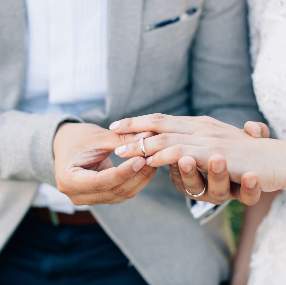groom putting ring on brides finger somewhere outdoors